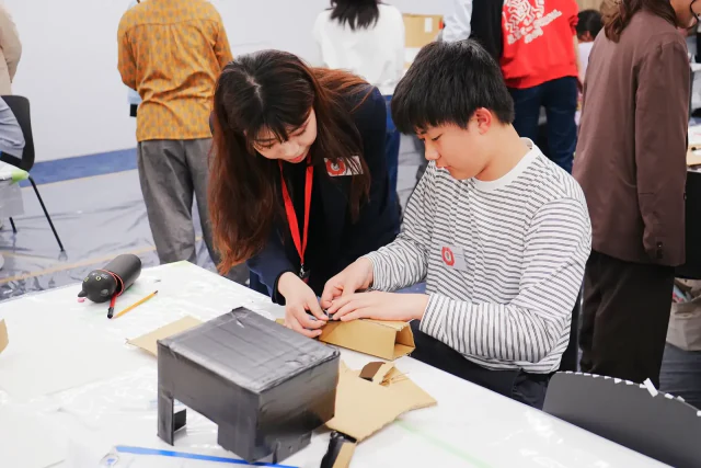 同じ机で一緒に手を動かし、段ボールでマスクをつくっている様子